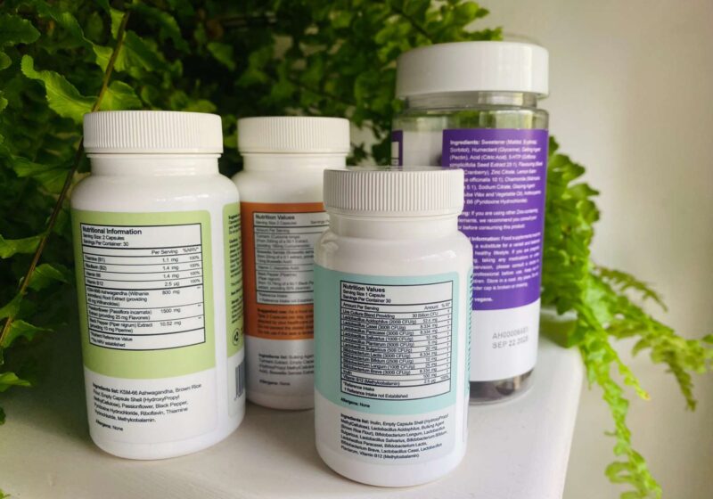 The ingredient lists of BetterVits supplements on a white surface infront of a green plant for this BetterVits review