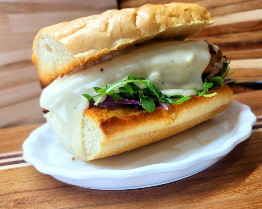Grilled chicken breast sandwich with melted cheese and greens on a French roll.