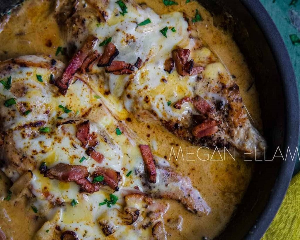Creamy chicken breast dish topped with bacon and herbs in a skillet.