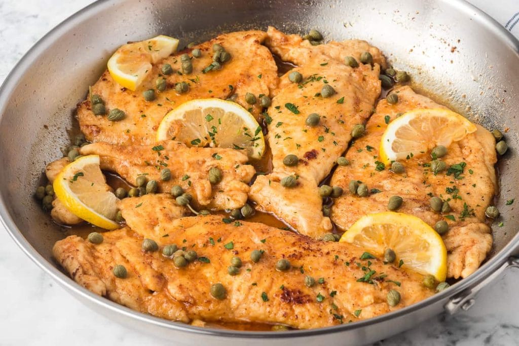 Chicken breast piccata with lemon slices and capers in a skillet.