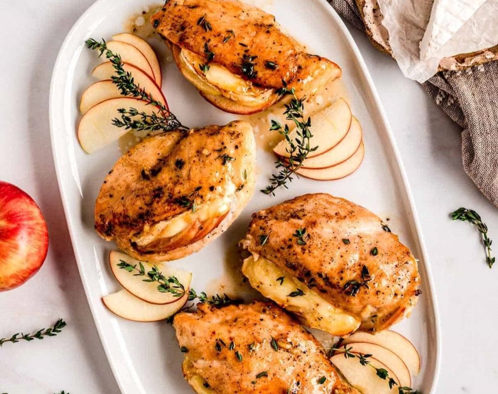 Herb-seasoned chicken breast recipes baked and served over sliced apples on a white oval plate.