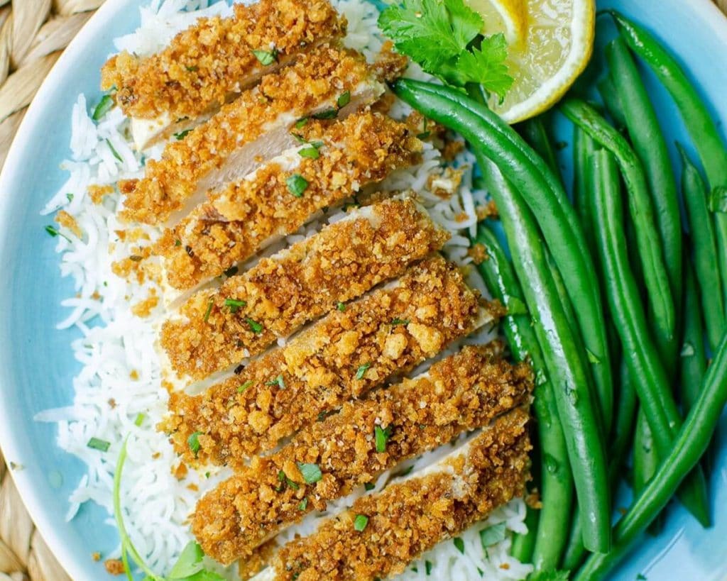 Sliced breaded chicken breast recipes served over rice with green beans and a wedge of lemon on the side.