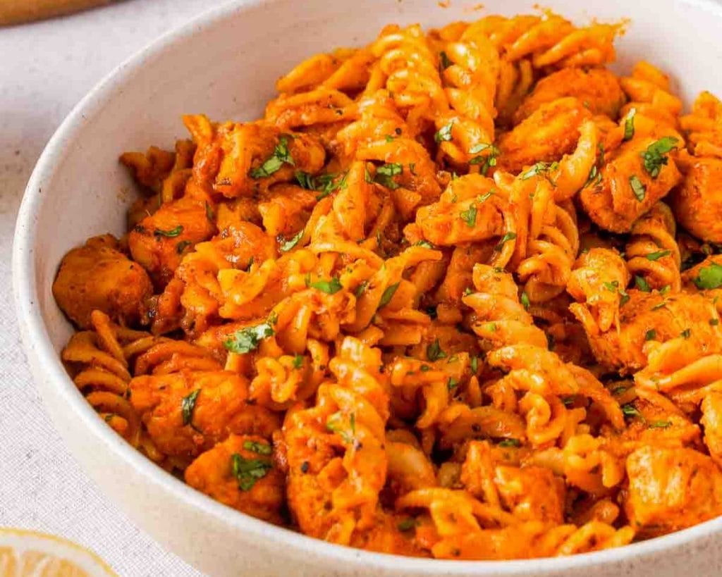 A bowl of creamy tomato pasta with chicken breast, sprinkled with fresh herbs.