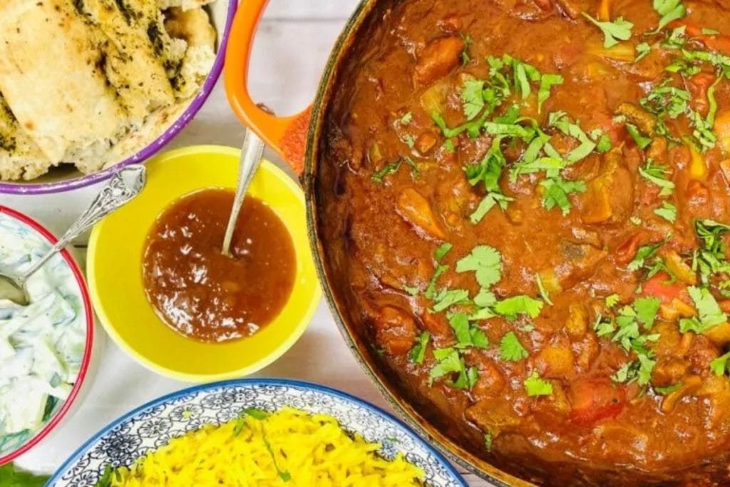 A vibrant Indian curry recipes meal featuring chicken curry, saffron rice, naan bread, raita, and mango chutney, garnished with fresh herbs.
