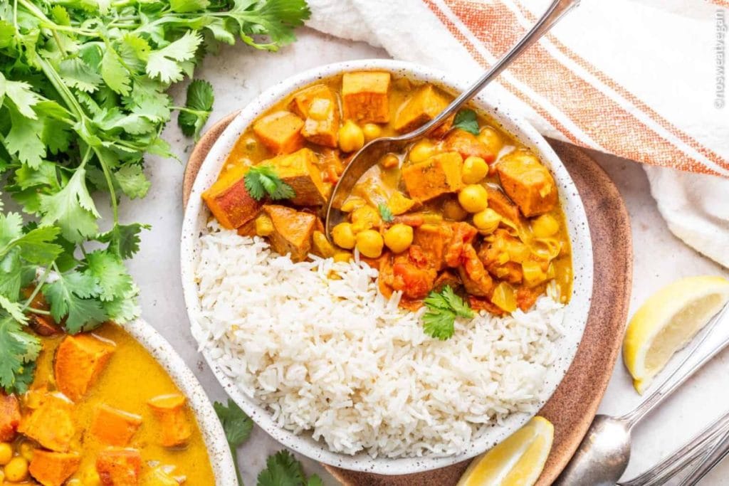 A bowl of chickpea and sweet potato curry recipes served with rice, garnished with fresh coriander.