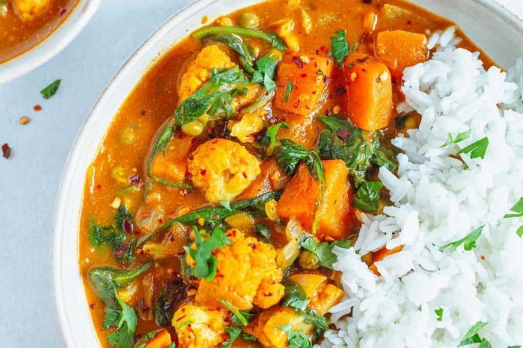 A bowl of creamy Curry Recipes with sweet potatoes and spinach served alongside white rice.