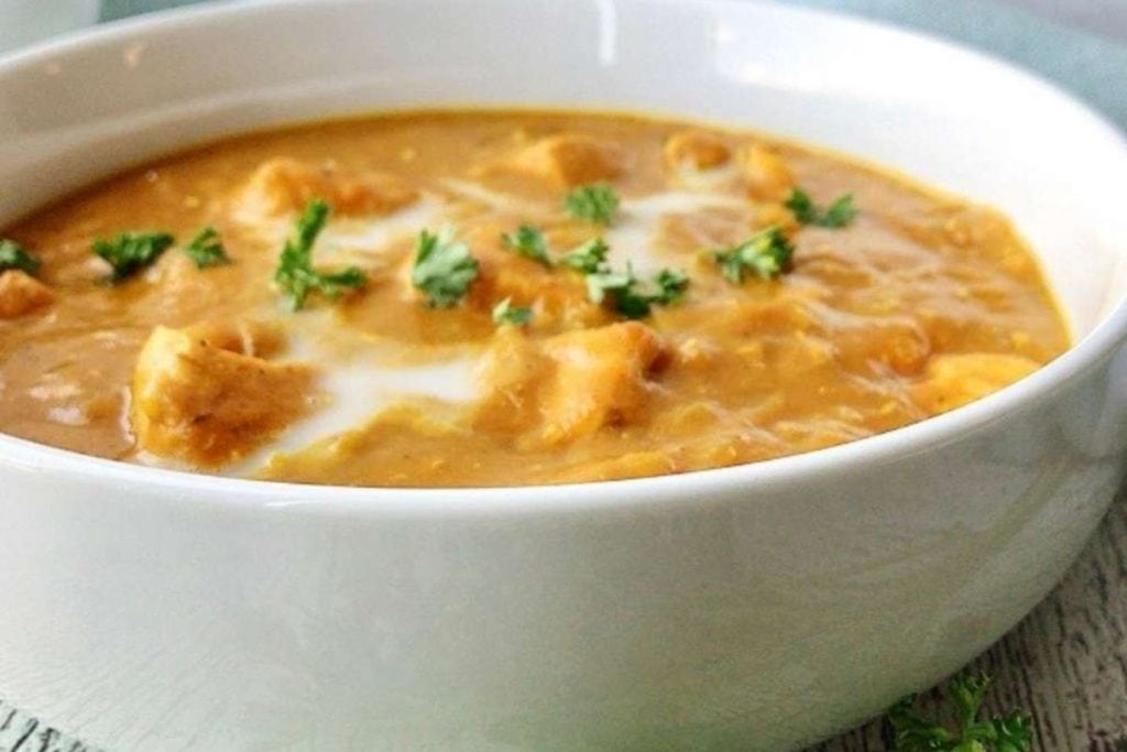 A bowl of creamy lentil curry soup garnished with fresh herbs.