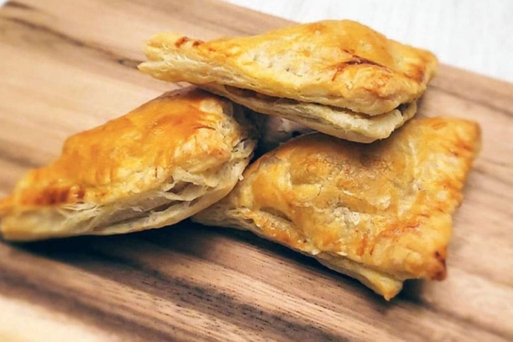 Three golden-brown curry puff pastries stacked on a wooden surface.