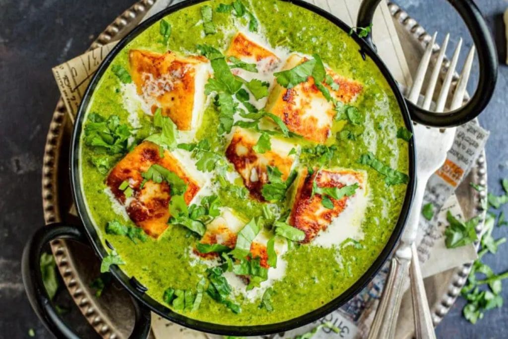 Paneer cubes in a creamy spinach curry, served in a black bowl.