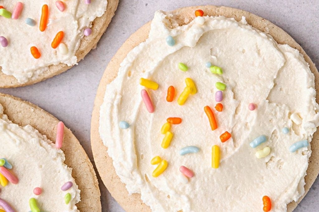 Three spring frosted cookies with colorful sprinkles on top.