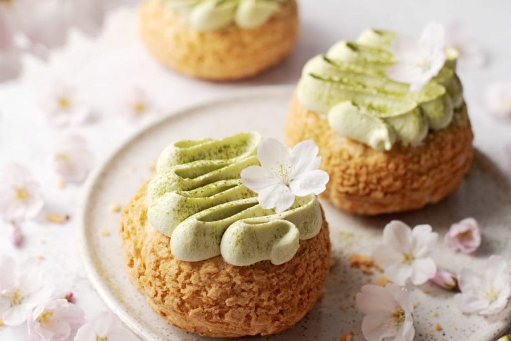 Elegant matcha-flavored spring desserts garnished with a white flower, presented on a plate with scattered cherry blossoms.