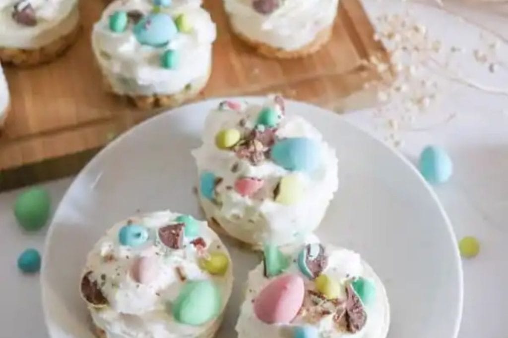 Spring-themed Easter cupcakes topped with frosting and colorful candy eggs on a white plate, with additional candies scattered around.