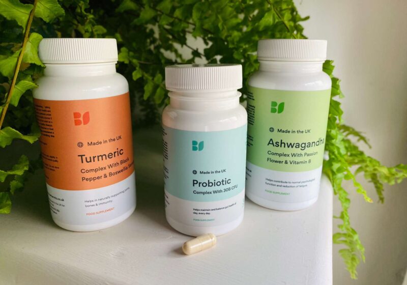 A selection of BetterVits supplements including their probiotic on a white surface infront of a green plant for this BetterVits review