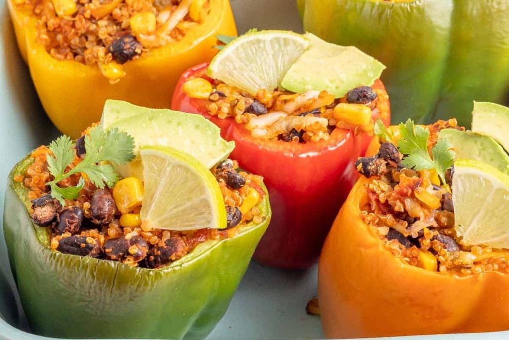 Stuffed bell peppers filled with quinoa, black beans, corn, and lime slices served in a dish.