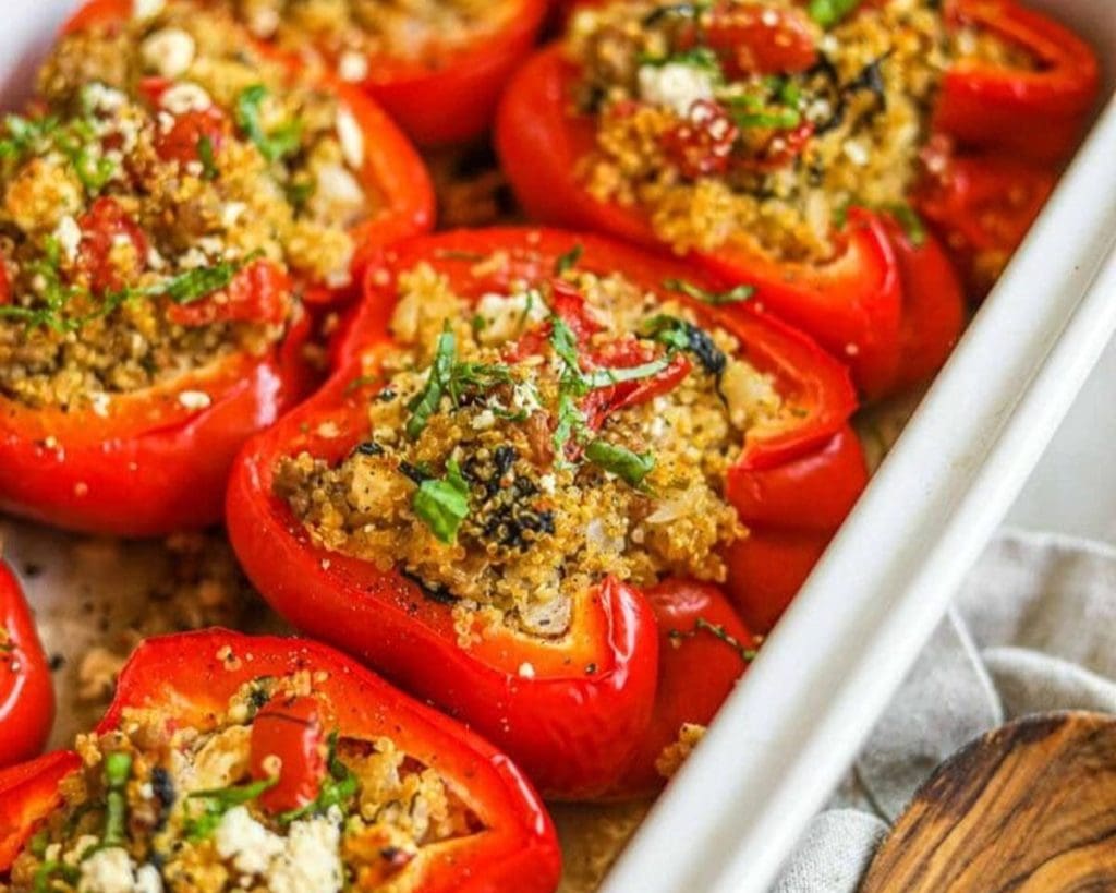 Cooked stuffed bell peppers filled with quinoa and garnished with herbs, served in a white baking dish.