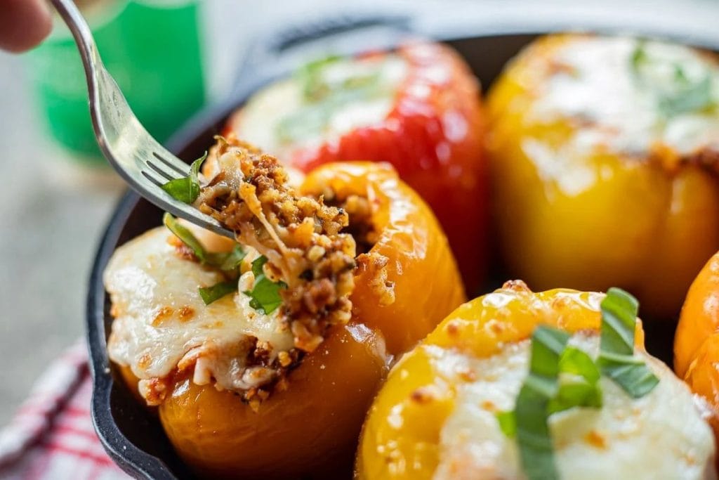 A close-up of a fork scooping out stuffed bell peppers filled with melted cheese and minced meat.