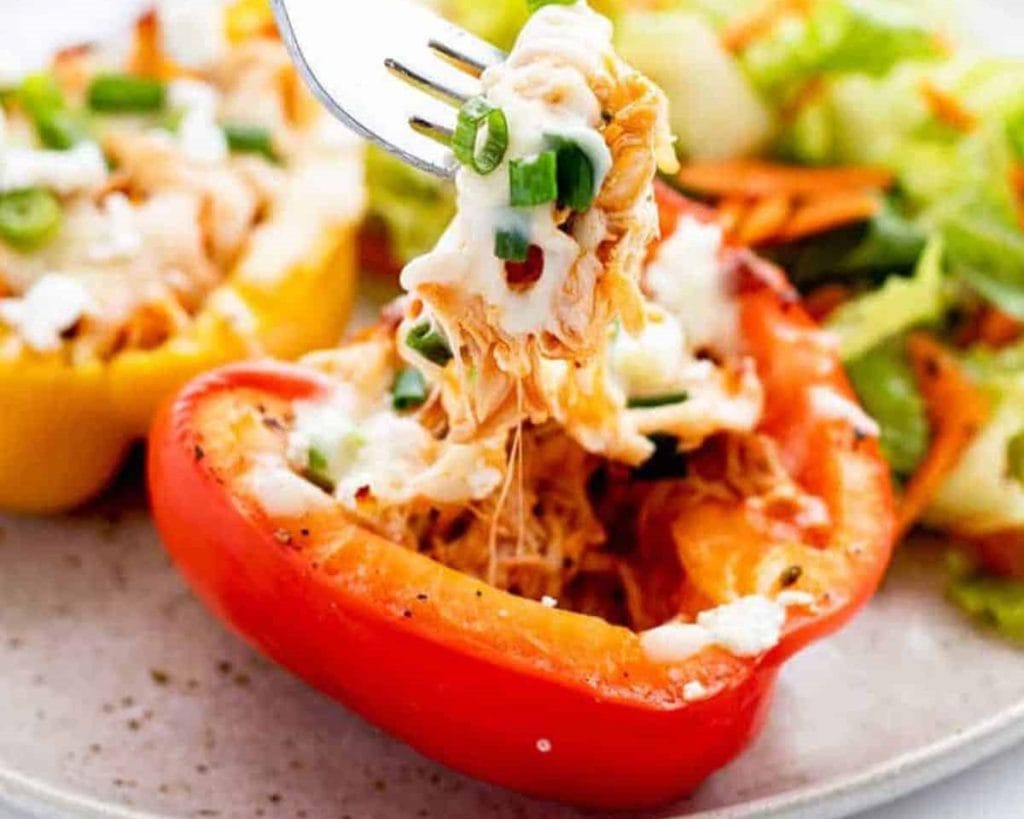 A close-up of stuffed bell peppers on a plate, with a fork lifting some of the creamy chicken filling.