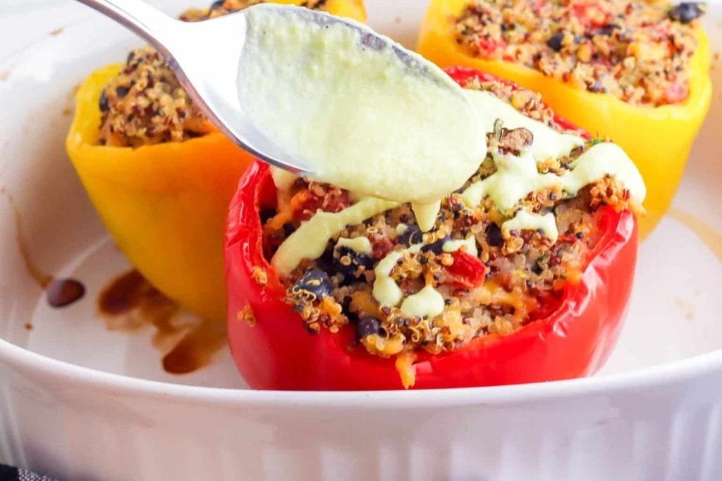 A spoon drizzling sauce over stuffed bell peppers in a white dish.