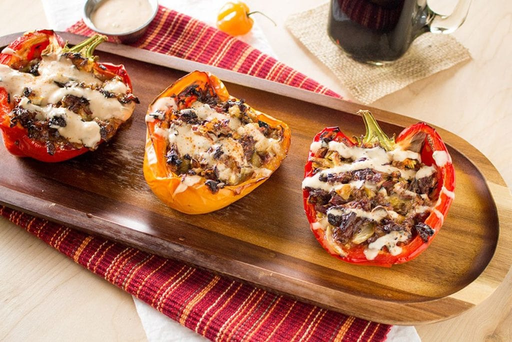 Three stuffed bell peppers filled with melted cheese, served on a wooden platter with a checkered red napkin and a glass of cola in the background.