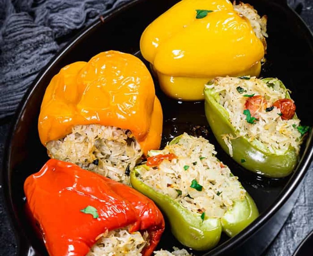 Stuffed bell peppers in red, yellow, and green, filled with rice and herbs in a black skillet, adorned with parsley.