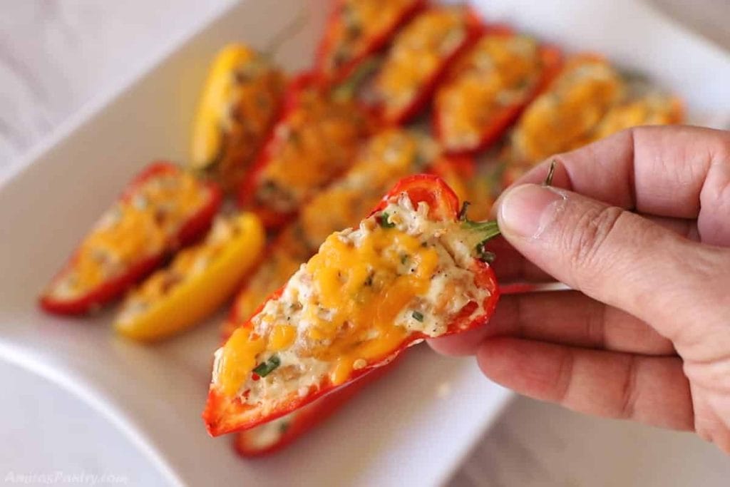 A person's hand holding a stuffed bell pepper over a plate of similarly prepared peppers.