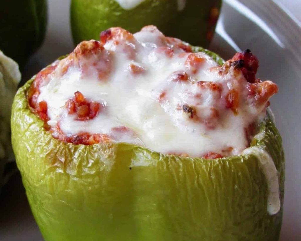 Three stuffed bell peppers filled with a mix of cheese and bacon, served on a white plate.