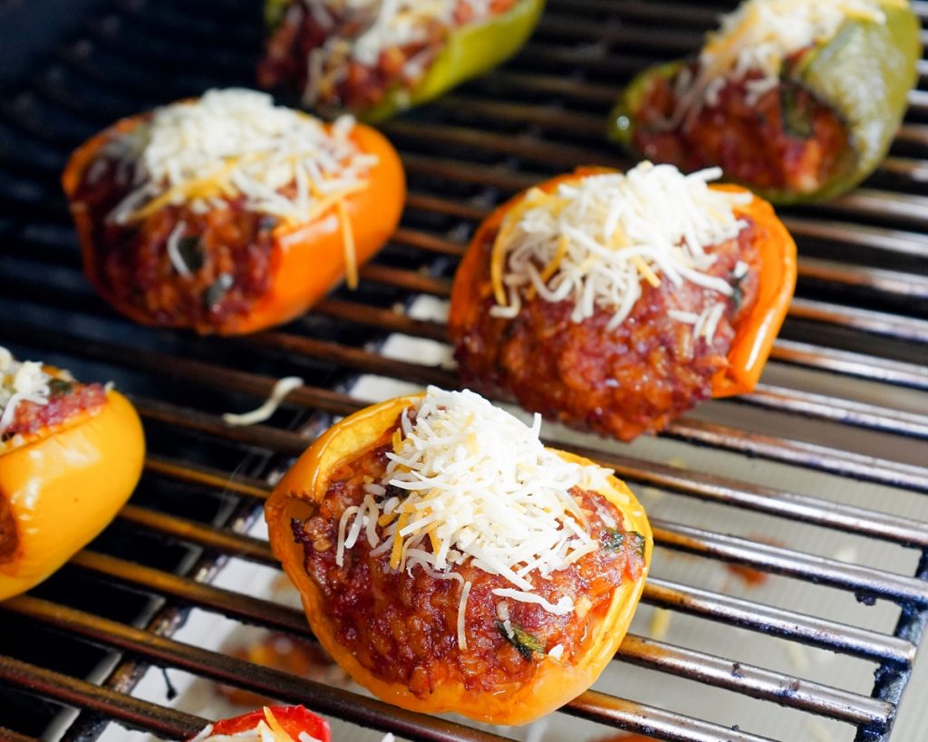 Stuffed bell peppers with melted cheese on top, grilling on a grill.