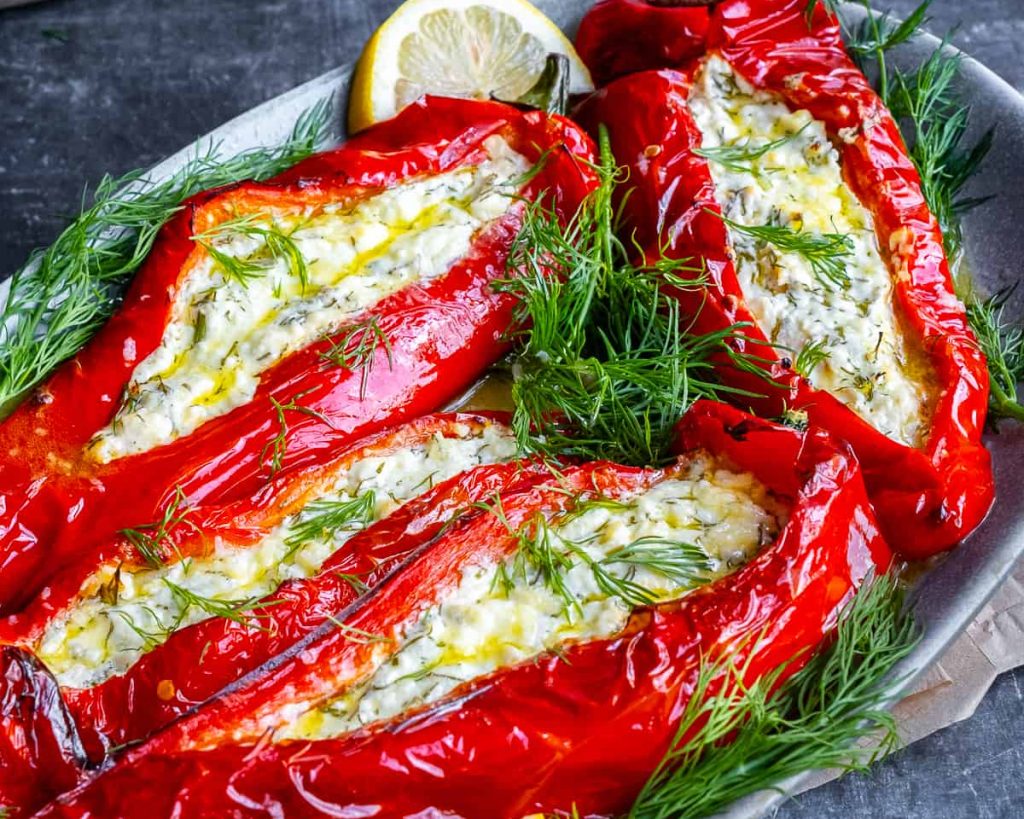 Stuffed bell peppers with cheese and herbs in a gray dish, garnished with dill and lemon slices.