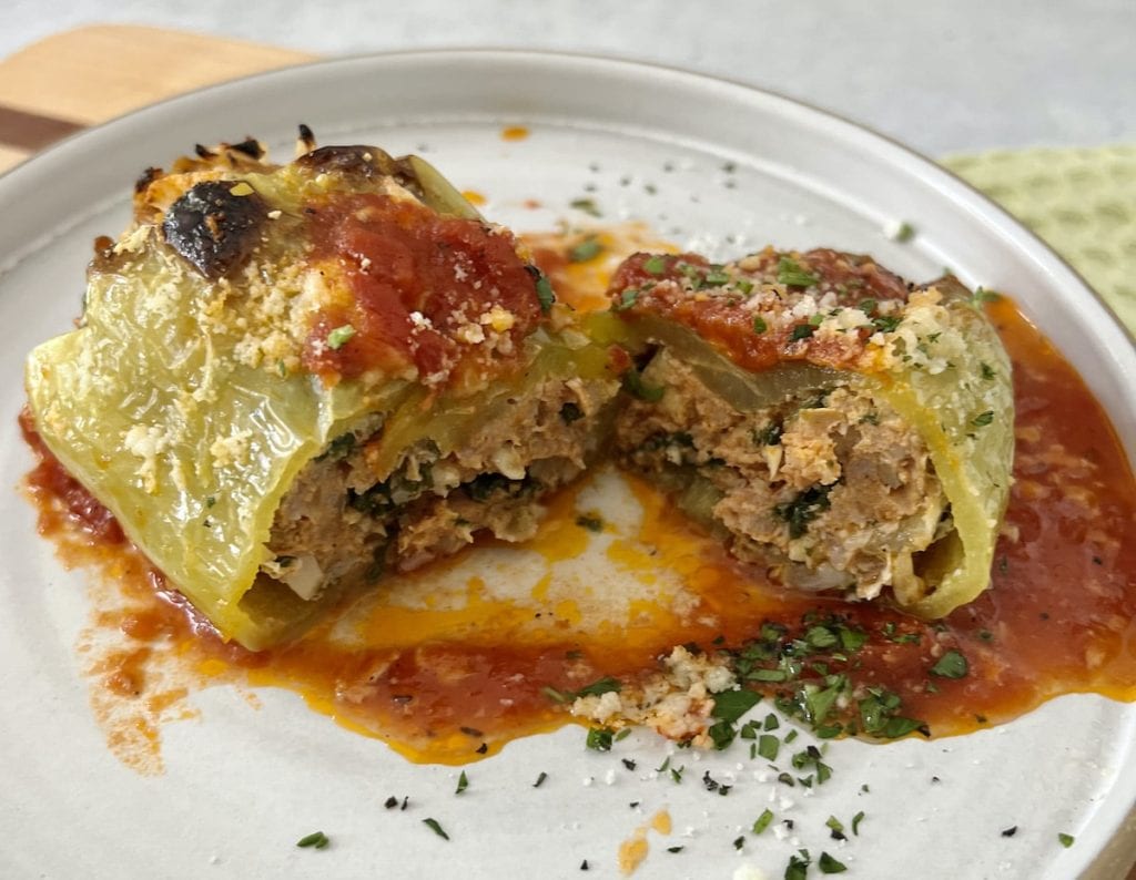 Stuffed bell peppers sliced in half on a plate, filled with meat and rice, topped with tomato sauce and parmesan, garnished with herbs.
